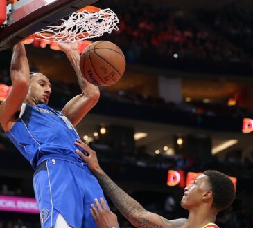 Dallas Mavericks forward Zaccharie Risacher hangs on the rim after a dunk as Houston Rockets forward Jabari Smith Jr. looks up.