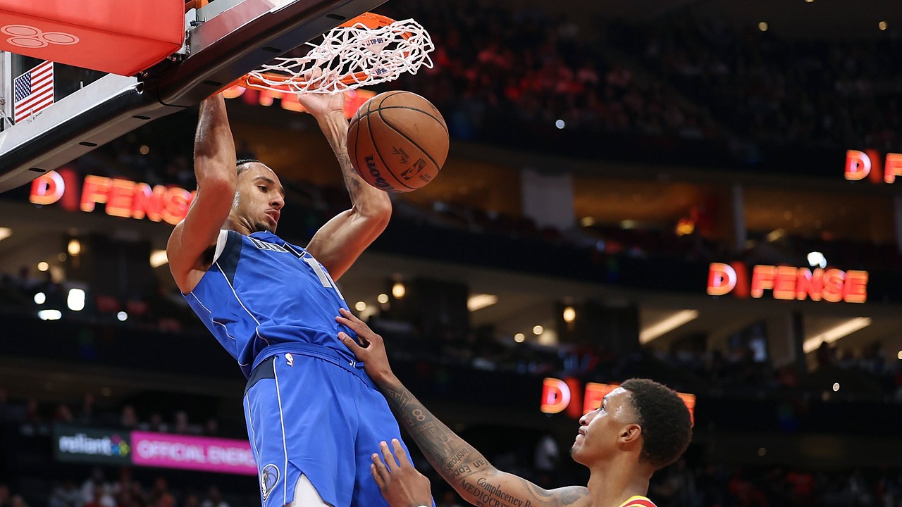 Dallas Mavericks forward Zaccharie Risacher hangs on the rim after a dunk as Houston Rockets forward Jabari Smith Jr. looks up.